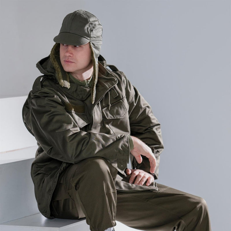 Man wearing genuine German Army olive drab winter pile cap with ear flaps and matching military jacket sitting indoors