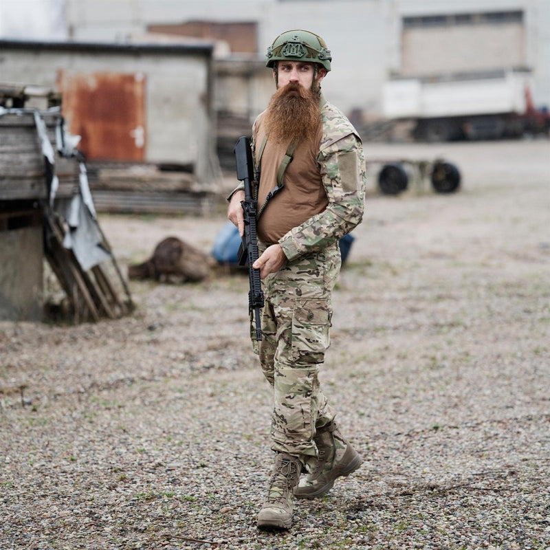 Man wearing Leo Kohler multicam tactical field pants and helmet holding a rifle in an outdoor urban environment