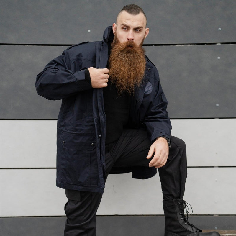 Man wearing original dark blue Dutch police military surplus parka jacket with hood standing against gray wall