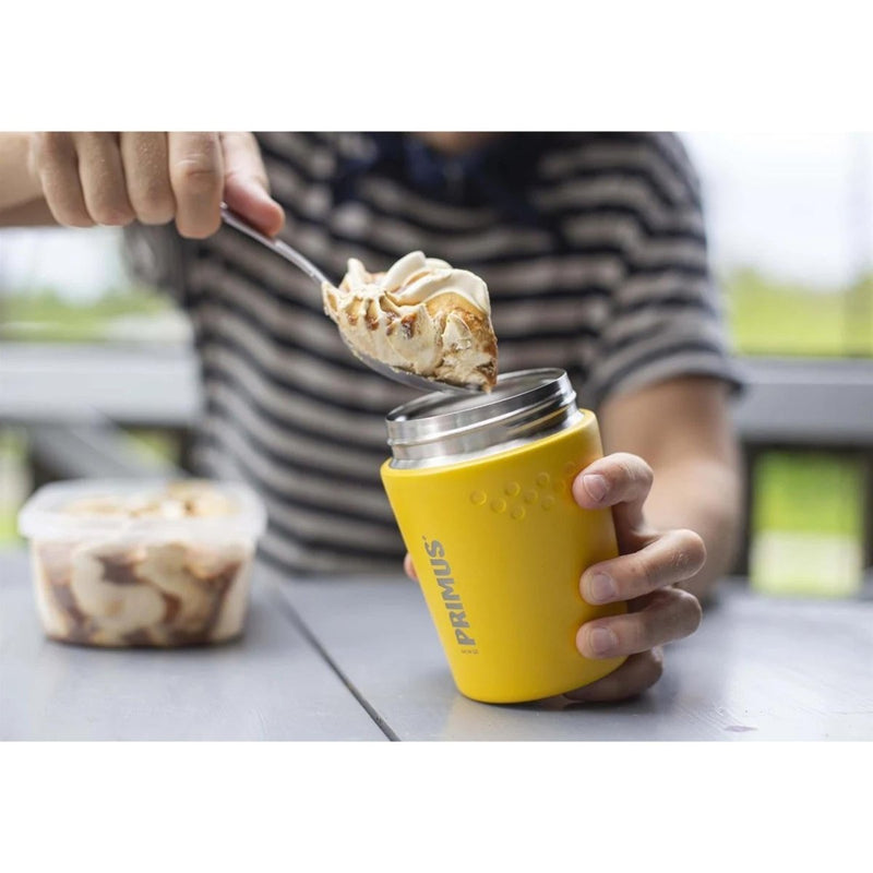 Person scooping food into a yellow Primus Trailbreak vacuum insulated jug on a table outdoors
